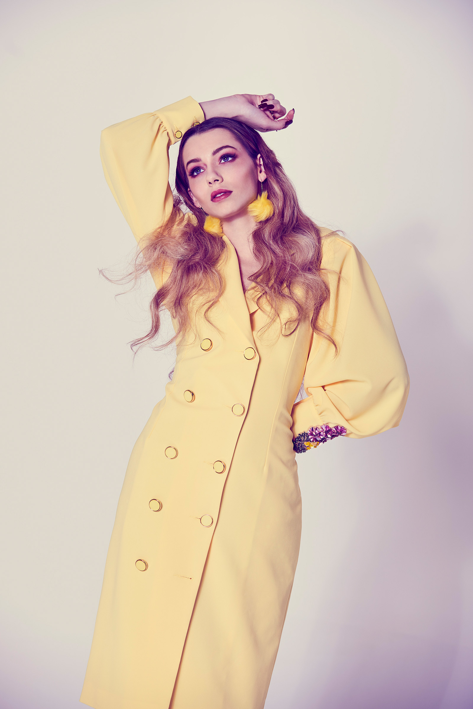 Studio retro fashion photography of female with long blonde hair wearing yellow double breasted long sleeve coat